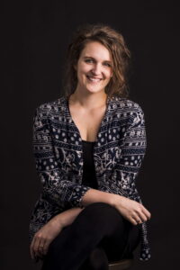 Portrait de Geneviève Albert, souriante, portant une veste à motifs noirs et blancs sur fond noir
