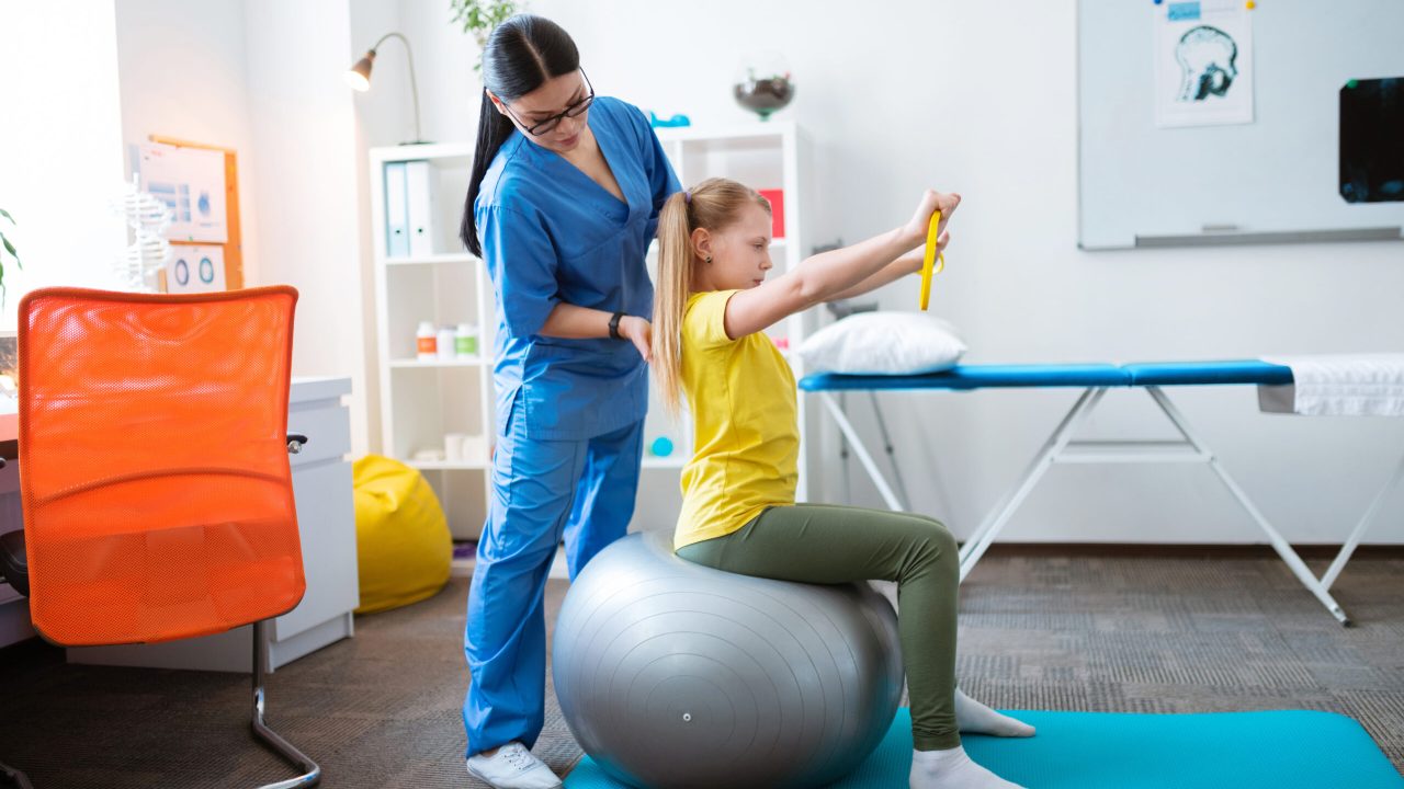 Concentrated long-haired therapist in blue uniform correcting posture