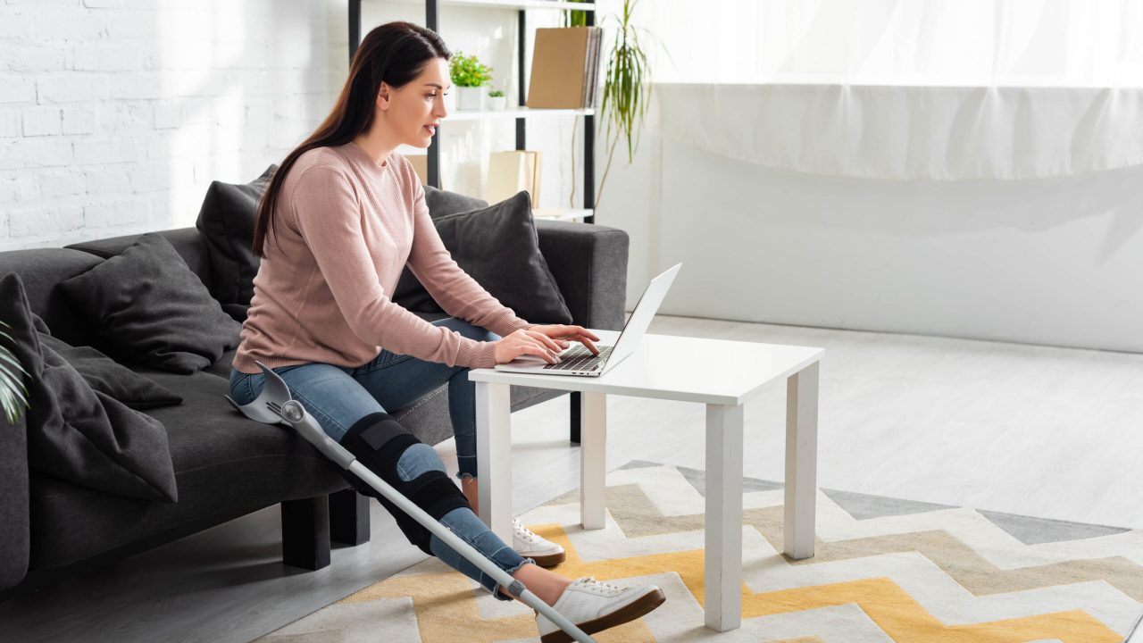 beautiful woman with broken leg having online consultation with doctor on laptop at home